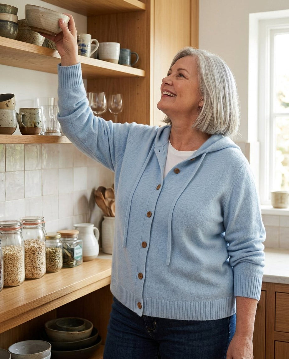 Woman with curves in the light blue Gillian cardigan reaching for a bowl on a high kitchen shelf